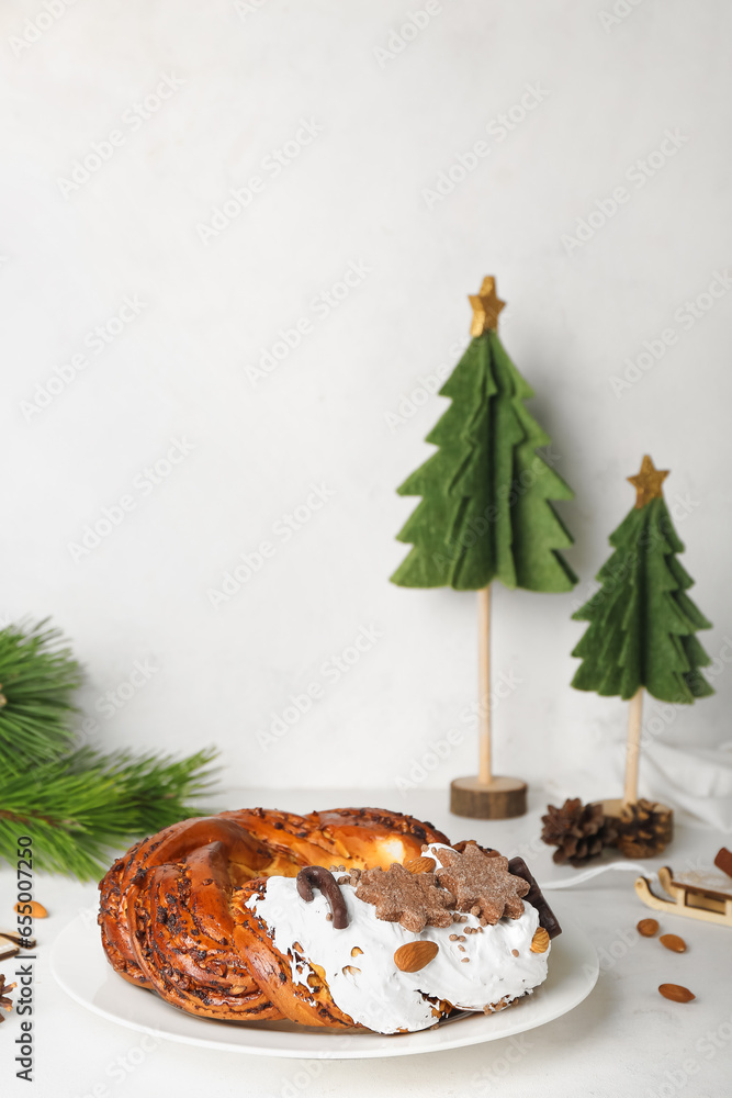 Plate with tasty Christmas pastry wreath and decorations on light background