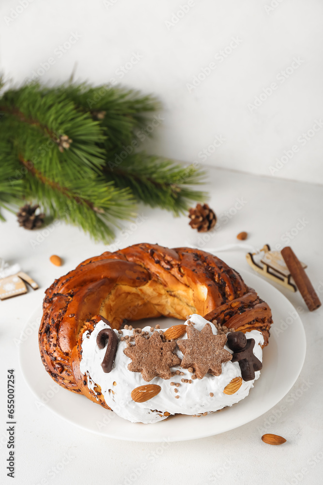 Plate with tasty Christmas pastry wreath and coniferous branch on light background