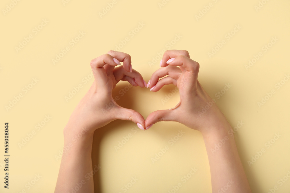 Woman making heart with her hands on beige background