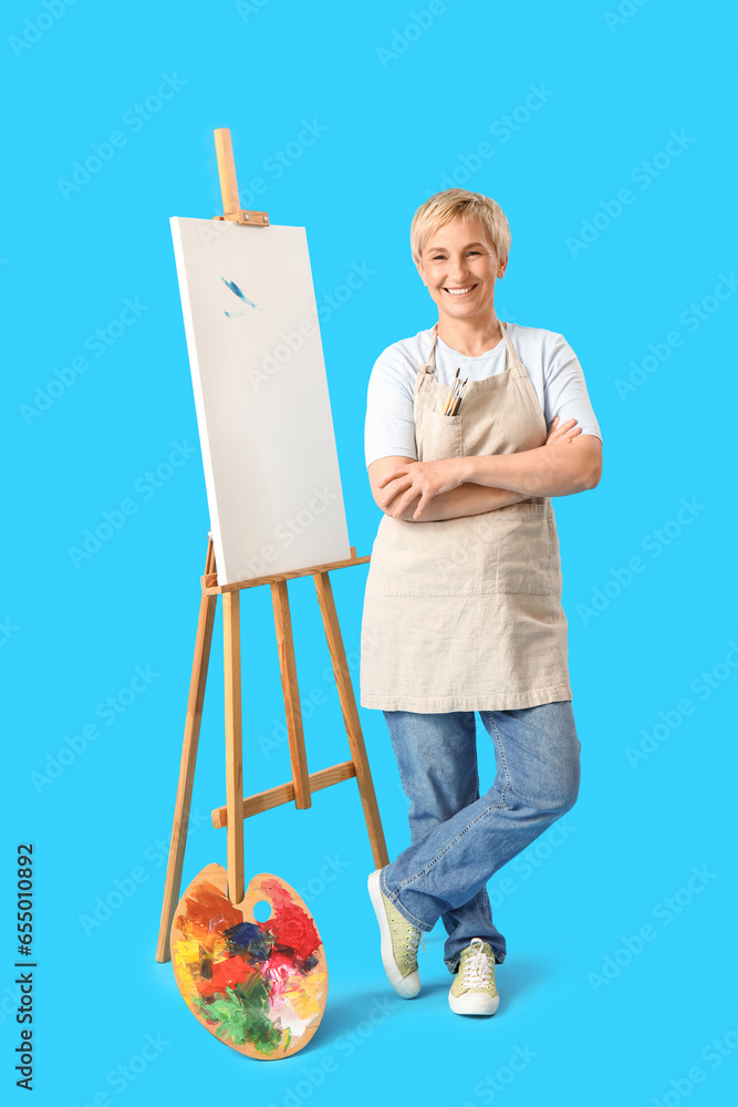 Mature female artist with tools and drawing easel on blue background