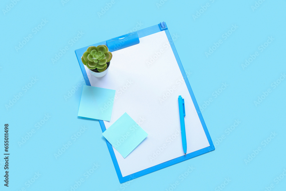 Blank open notebook with pen, sticky notes and houseplant on blue background