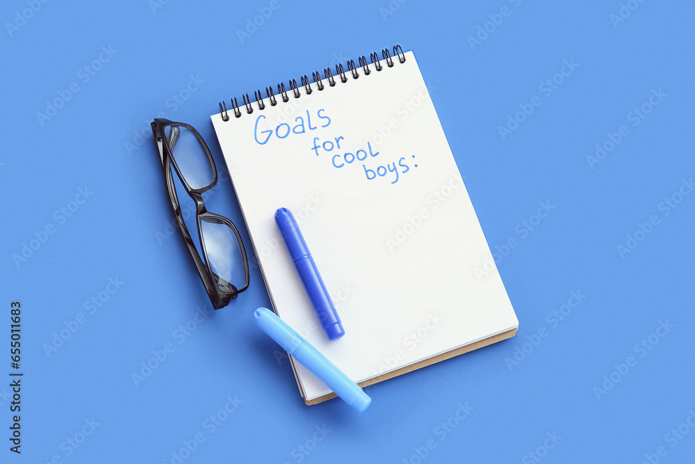 Notebook with empty to do list, markers and eyeglasses on blue background. New year goals