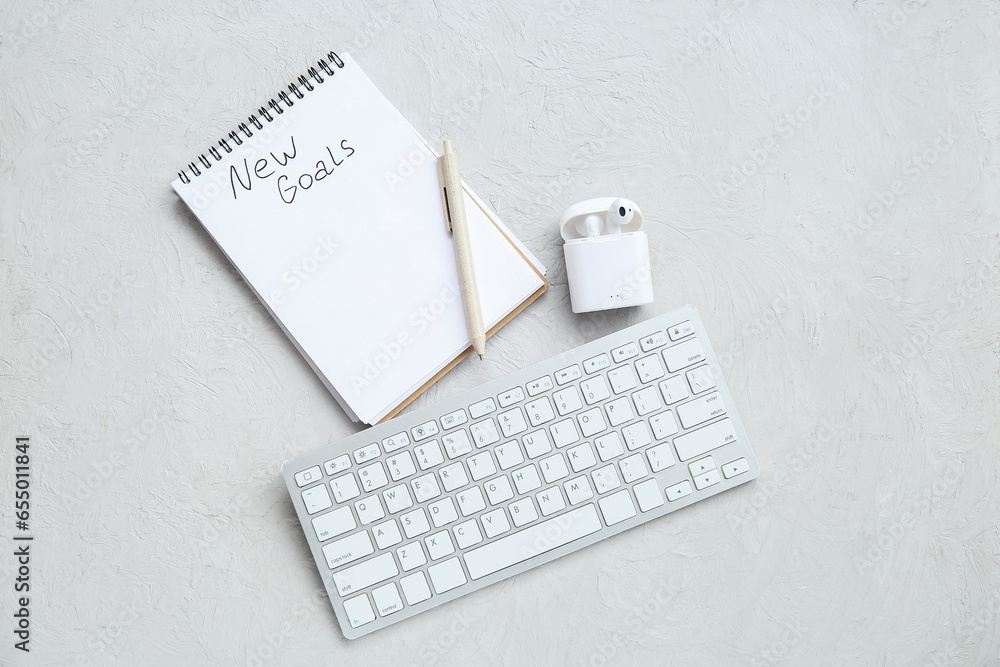 Notebook with empty to do list, earphones and keyboard on white textured background. New year goals