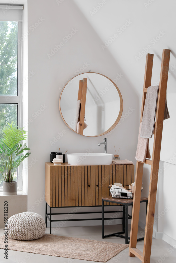 Sink bowl and bath accessories on wooden cabinet in interior of light bathroom