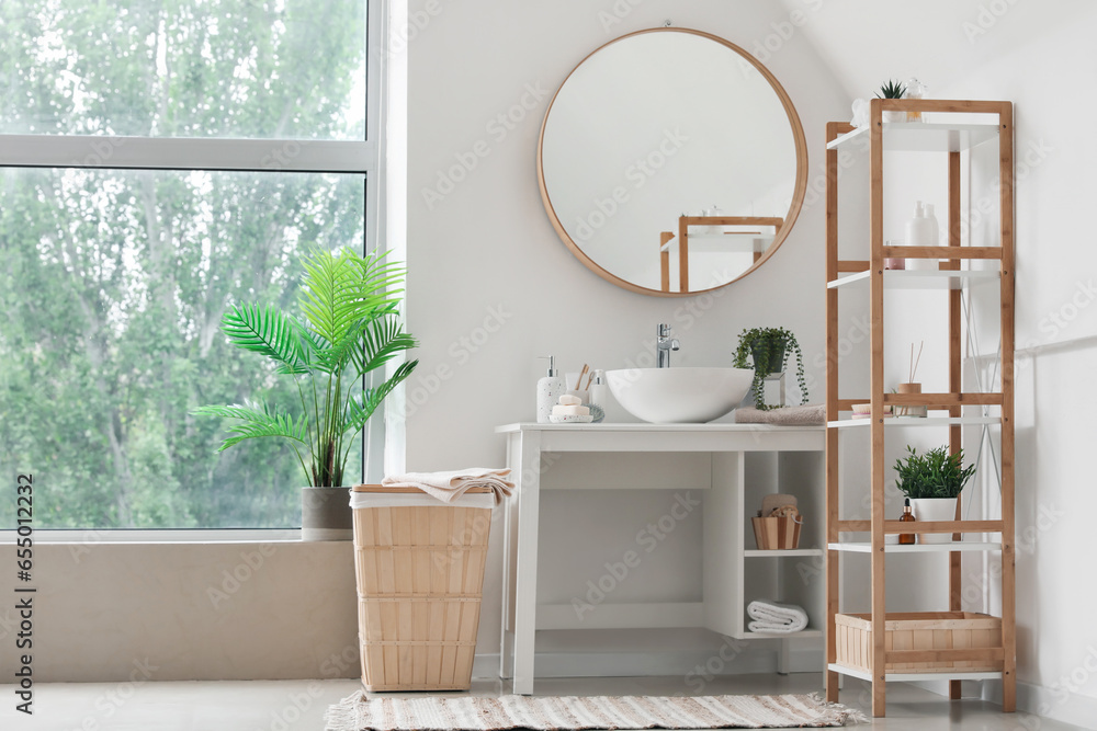 Interior of light bathroom with sink bowl, bath accessories, mirror and shelving unit