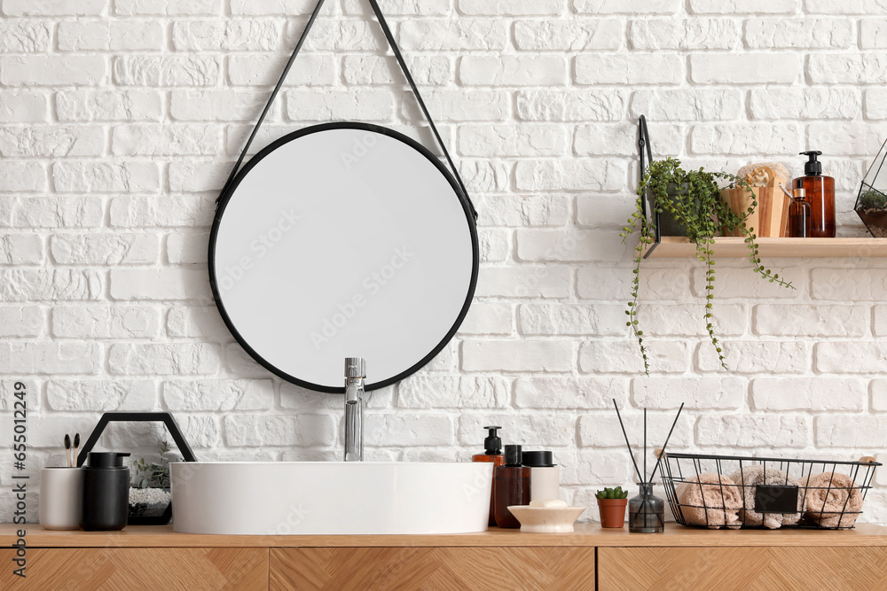 Sink bowl and bath accessories on wooden cabinet near white brick wall