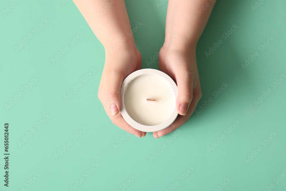 Female hands holding candle on turquoise background