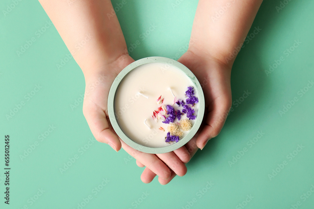 Female hands holding candle with flowers on turquoise background