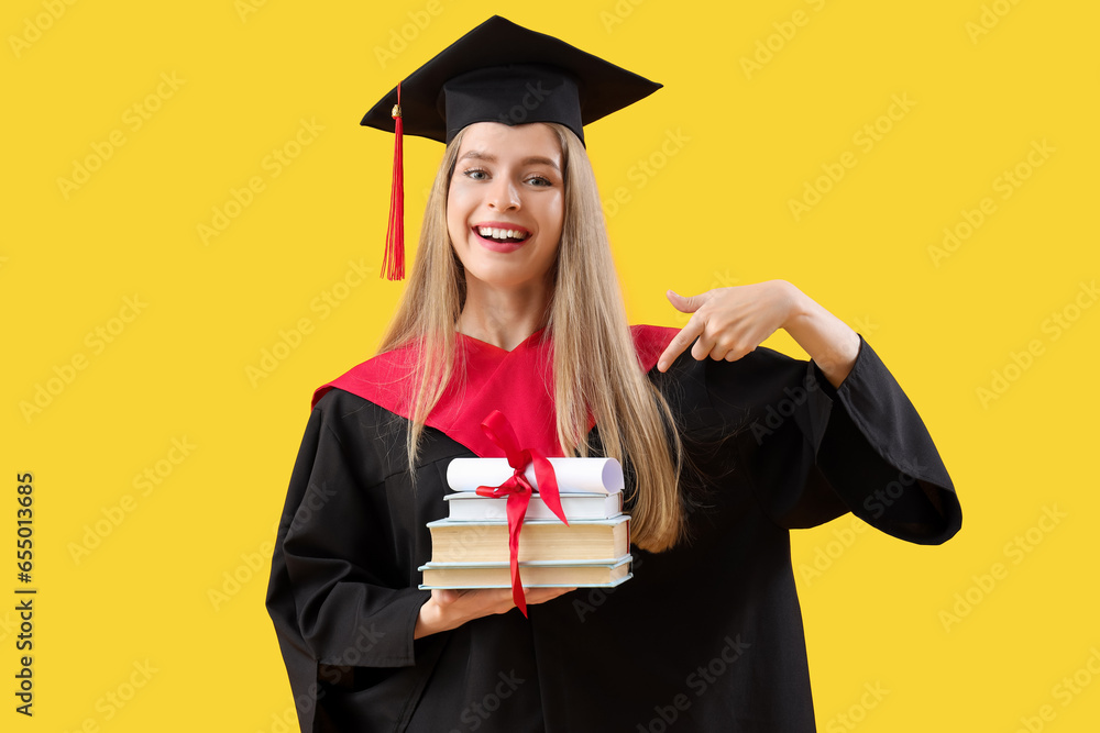 Female graduate student pointing at diploma and books on yellow background