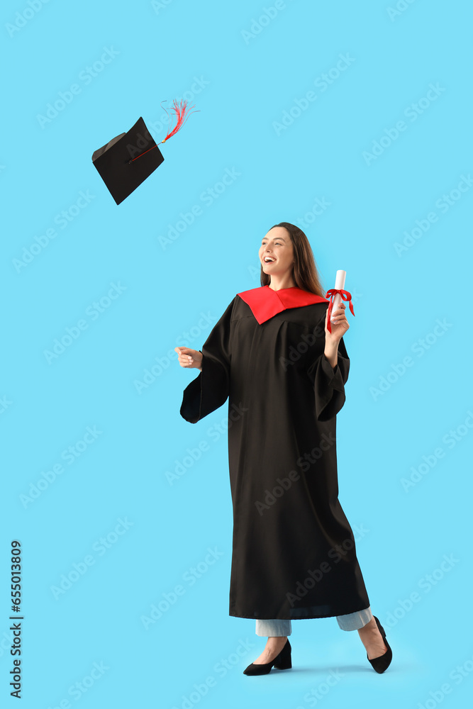 Female graduate student with diploma throwing her cap on blue background