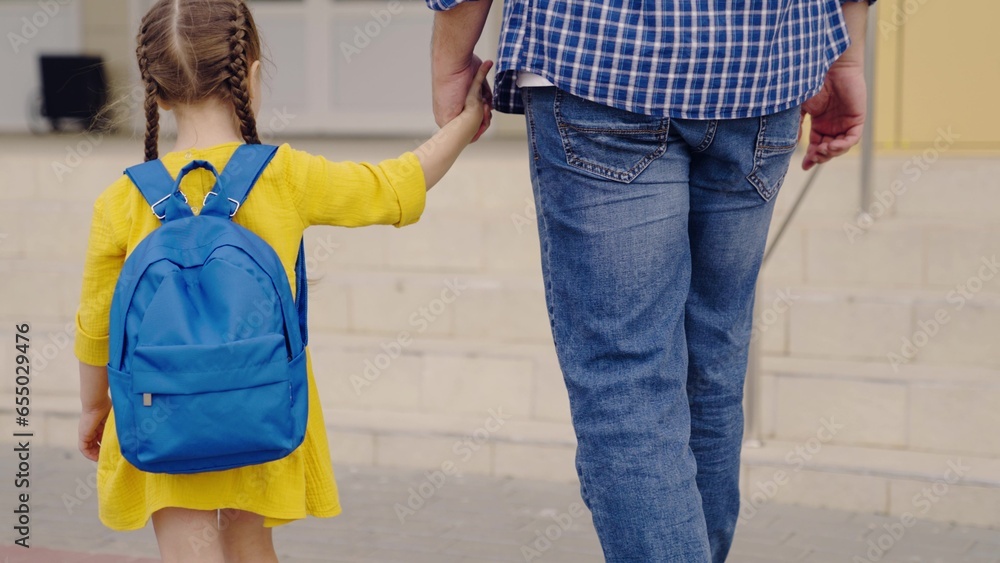 Happy family, dad daughter walk down street hand in hand to school. Little girl goes with her father to school for first lesson, dream about school. Father, kid girl carry his daughter school backpack