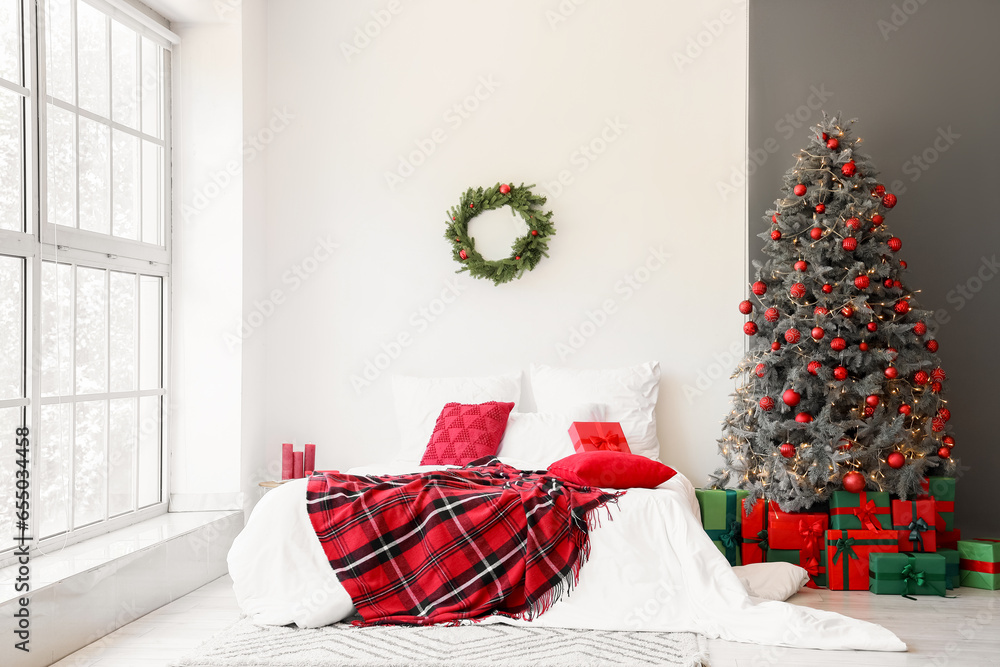 Interior of festive bedroom with comfortable bed, wreath and Christmas tree