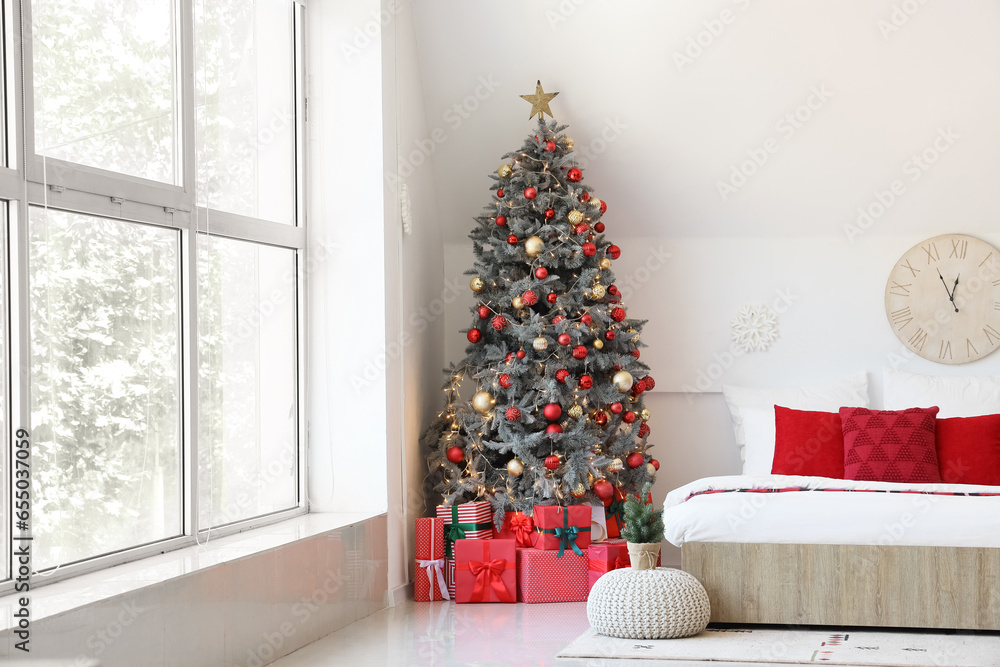 Interior of festive bedroom with comfortable bed and Christmas tree