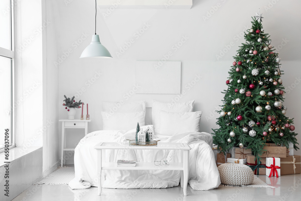 Interior of festive bedroom with comfortable bed and Christmas tree