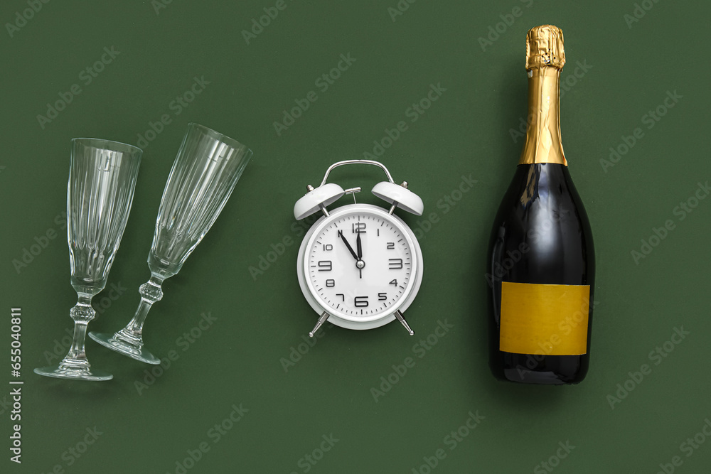 Alarm clock with champagne and glasses on green background