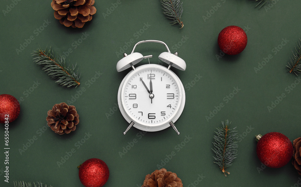 Alarm clock with Christmas tree branches and balls on green background