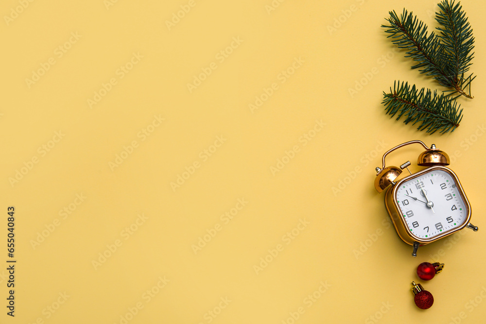 Alarm clock with Christmas tree branches and balls on yellow background