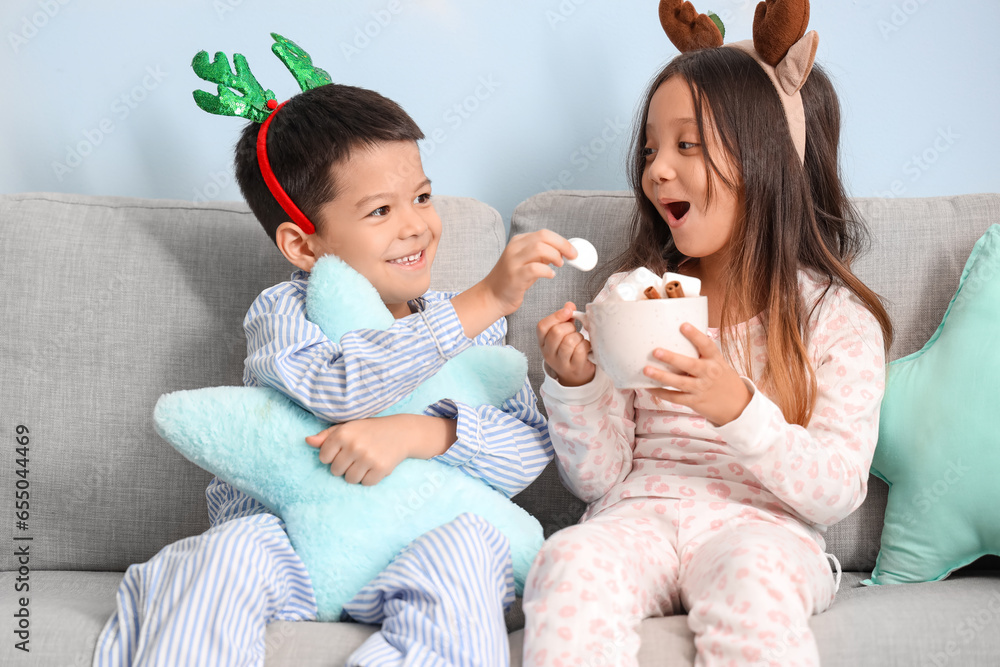 Cute little children in pajamas and with cup of tasty hot chocolate on Christmas eve at home