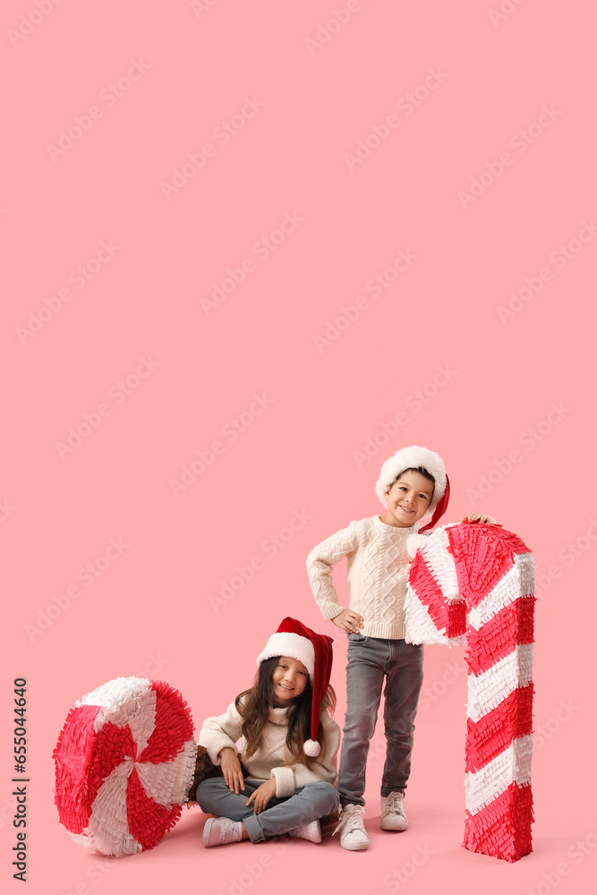 Cute little children with Christmas pinatas on pink background