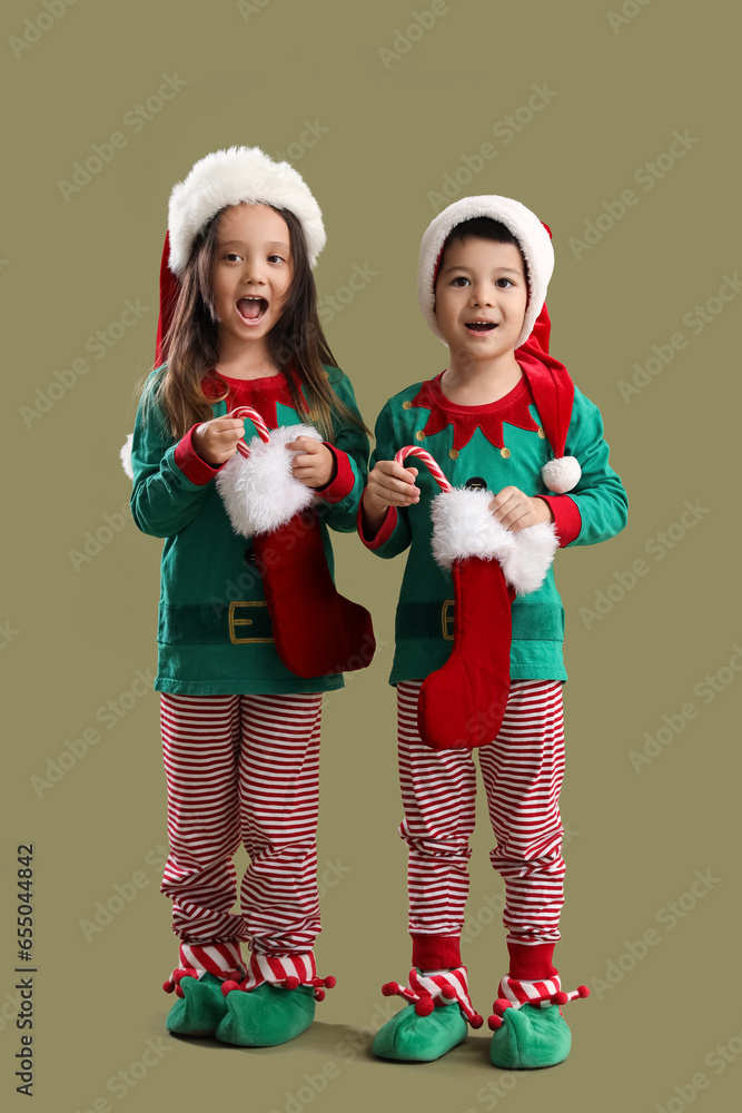 Surprised little children in elfs costumes, with Santa Claus socks and candy canes on green background