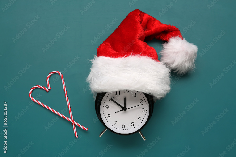 Composition with alarm clock, Santa hat and candy canes on color background