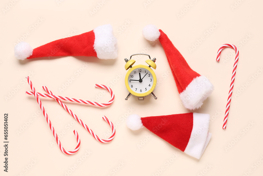 Composition with alarm clock, Santa hats and candy canes on color background