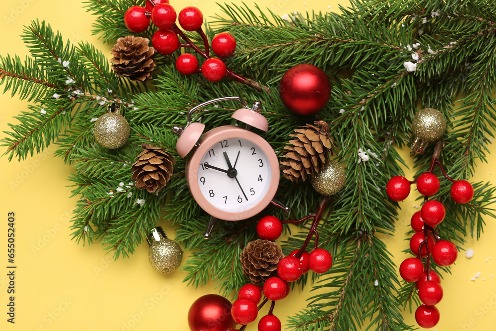 Alarm clock and Christmas tree branches with balls on yellow background