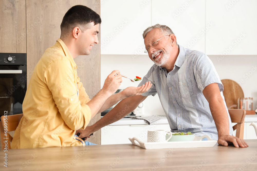 Young man feeding his father in kitchen