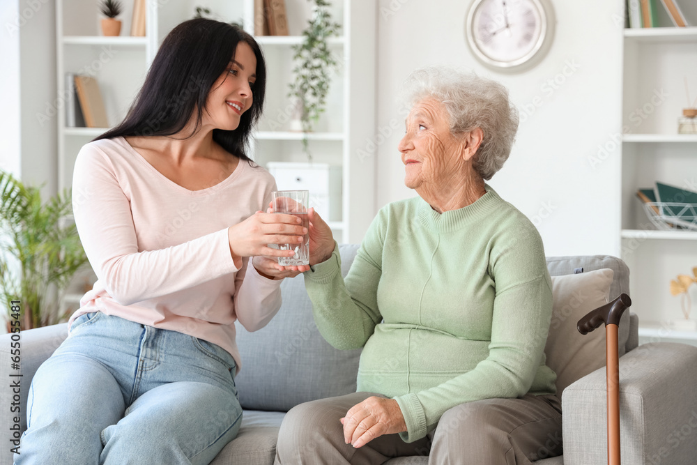 Senior woman taking glass of water from her daughter at home