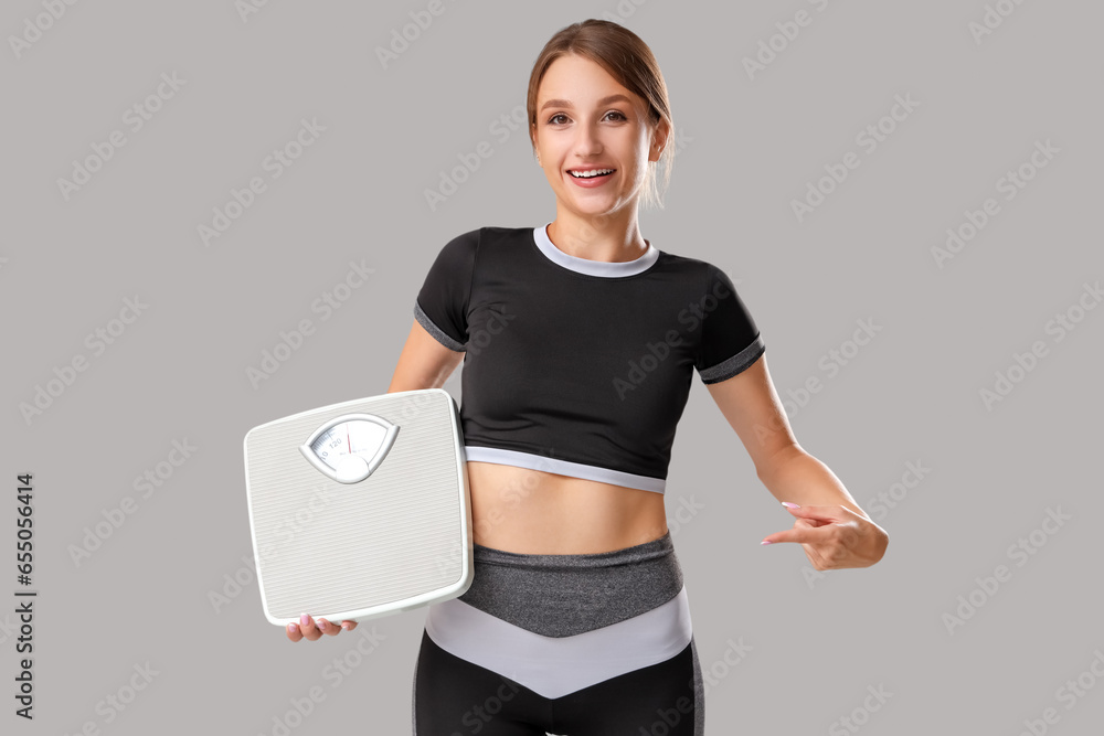 Beautiful young woman pointing at scales on grey background. Weight loss concept