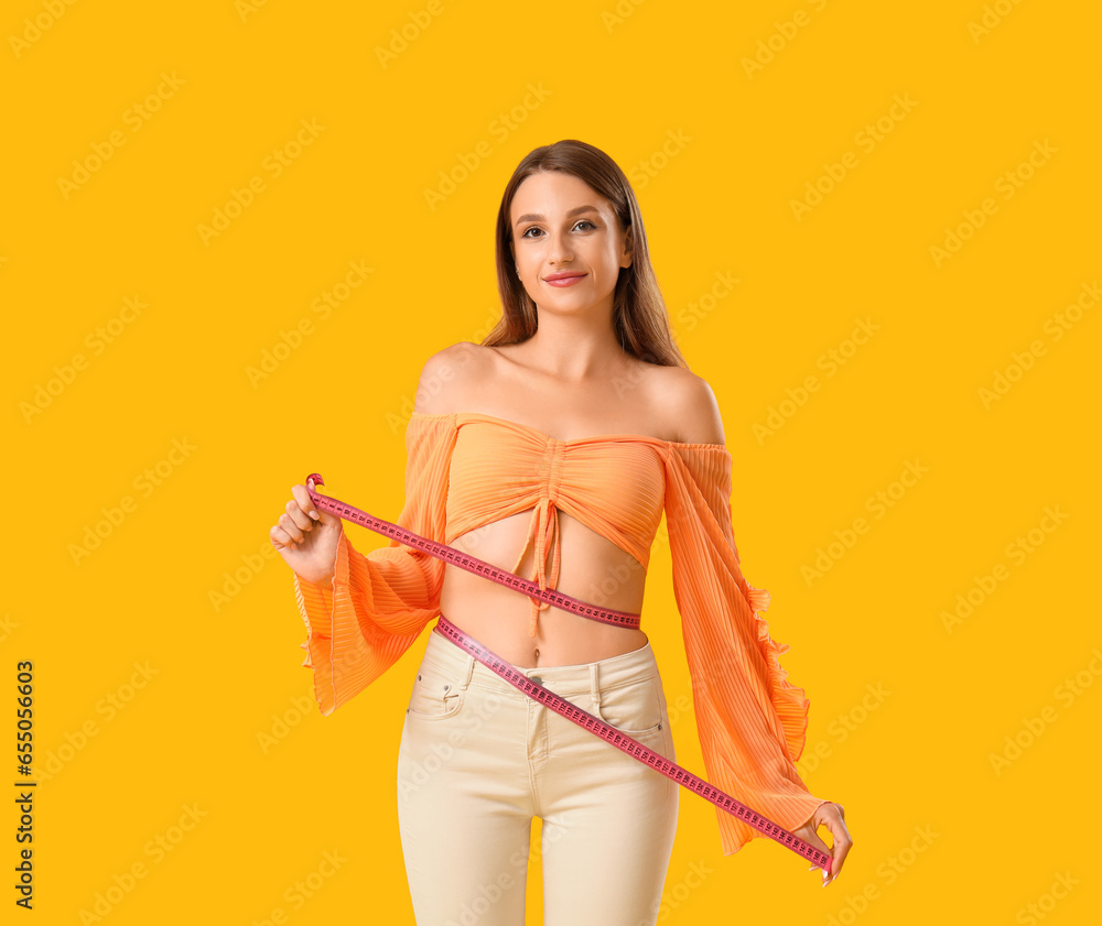 Beautiful young woman measuring her waist on yellow background. Weight loss concept