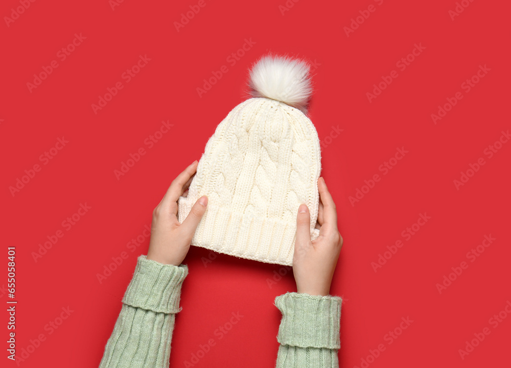 Female hands with knitted warm hat on red background, closeup