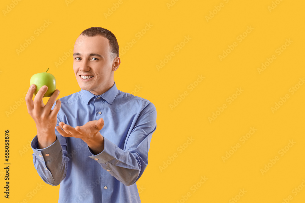 Young man with tasty apple on yellow background