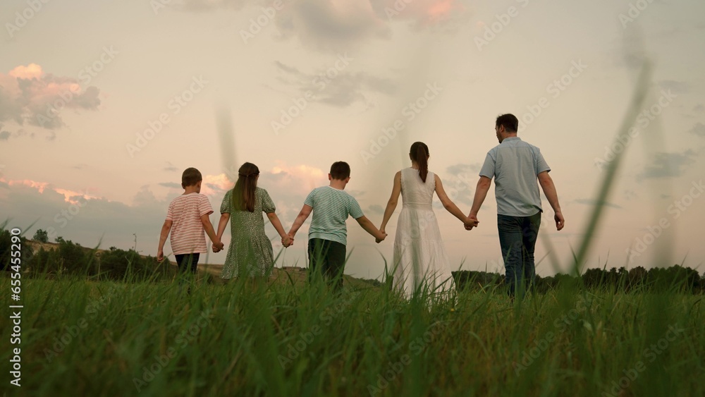 Active family with children walks in grass field in summer against sky. Family, Dad mom daughter son go hand in hand outdoors in autumn. Big family, group of people, nature. Parental care for children