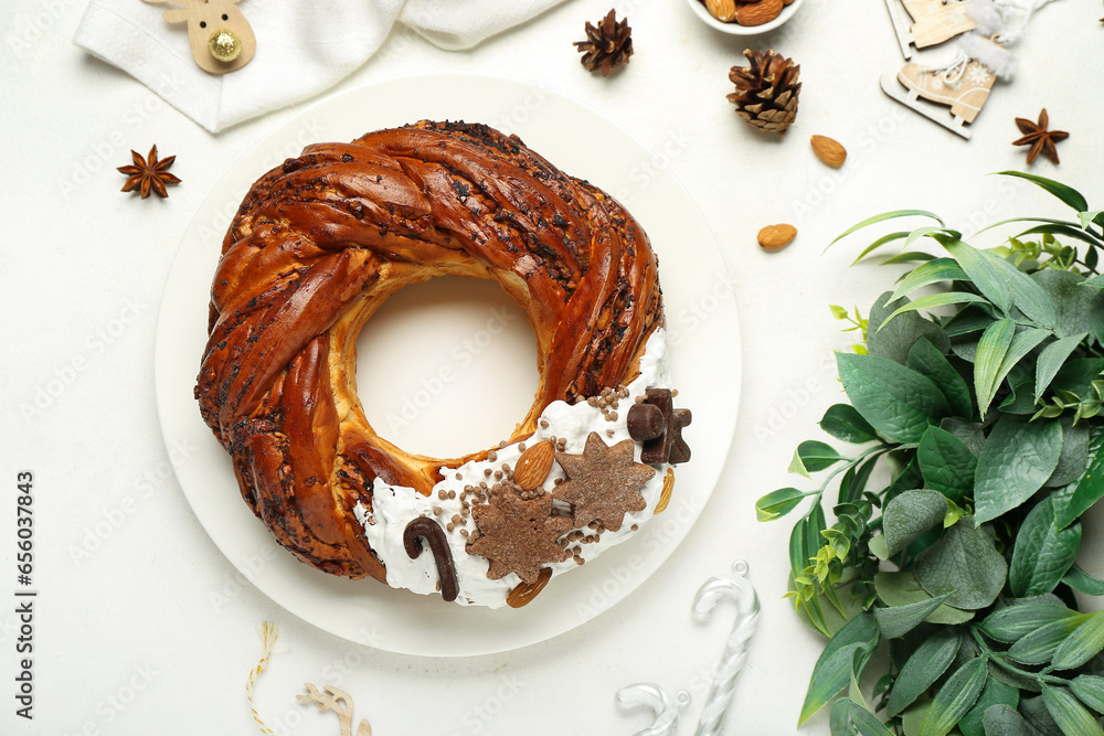 Plate with tasty Christmas pastry wreath and decorations on light background