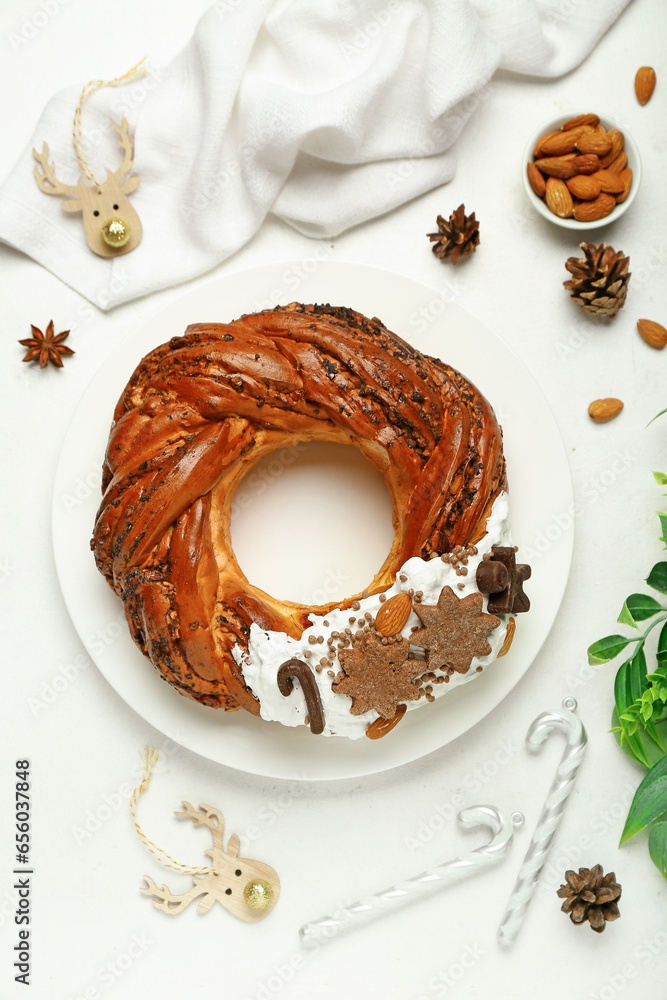 Plate with tasty Christmas pastry wreath and decorations on light background