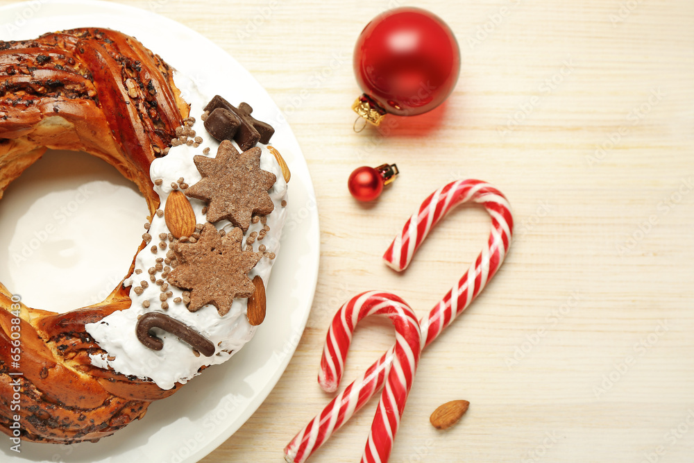 Plate with tasty Christmas pastry wreath, candy canes and balls on wooden background