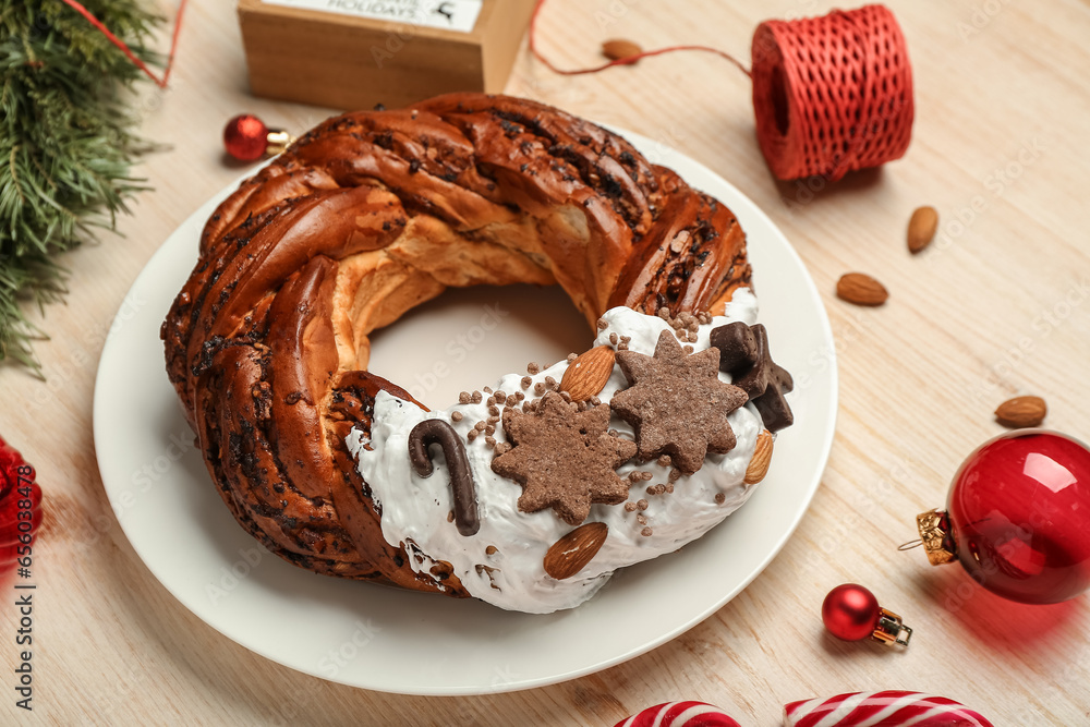 Plate with tasty Christmas pastry wreath and decorations on wooden background