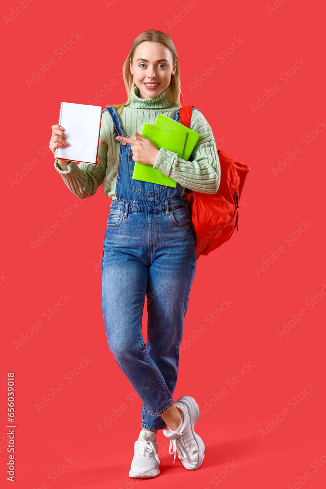 Female student pointing at notebook on red background