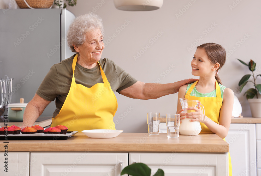 Senior woman and her little granddaughter with jug of milk in kitchen