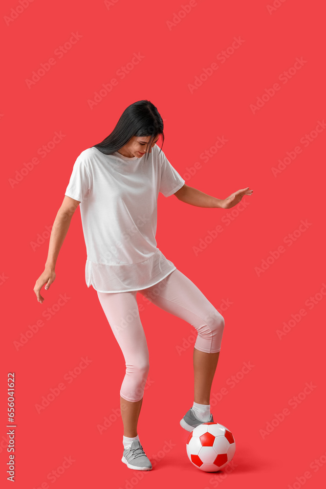 Young woman playing with soccer ball on red background