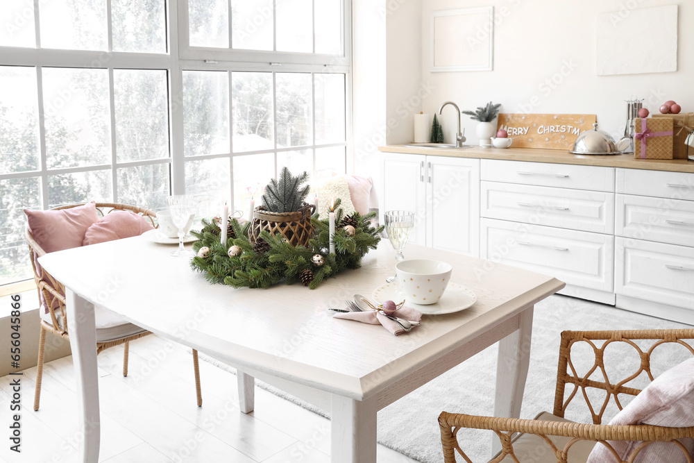 White dining table with champagne glasses, burning candles and Christmas wreath in kitchen