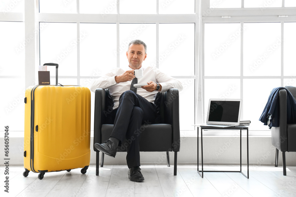 Mature businessman with cup of coffee sitting in hall of airport