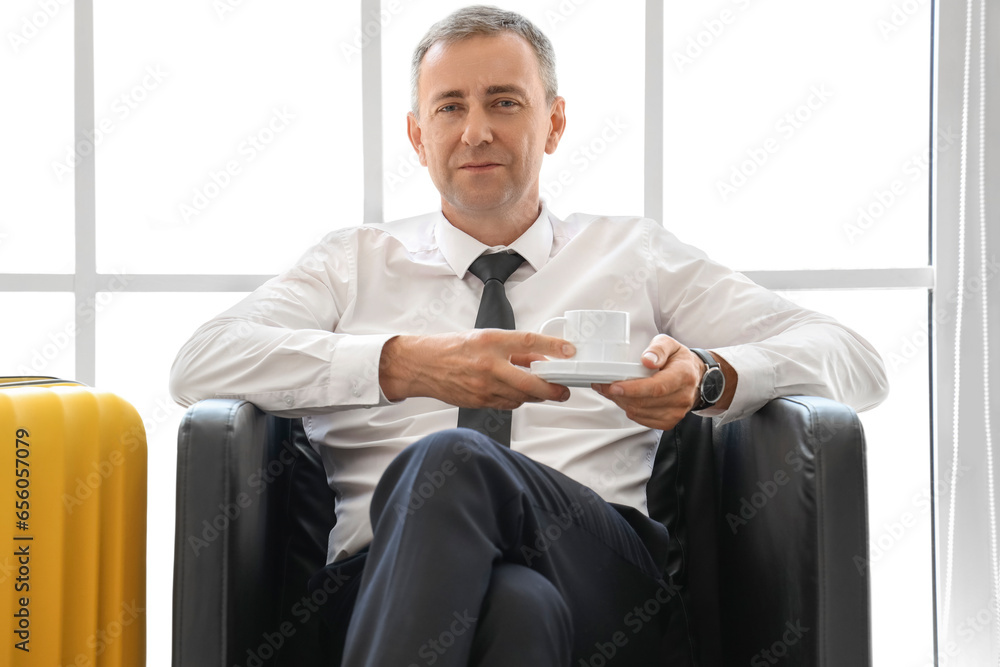 Mature businessman with cup of coffee sitting in hall of airport