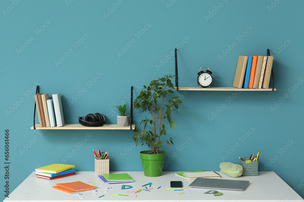 Modern school desk with stationery in room near blue wall