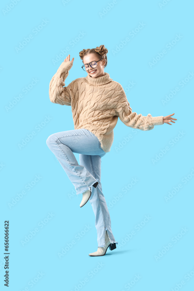 Happy beautiful young woman in warm sweater and eyeglasses on blue background