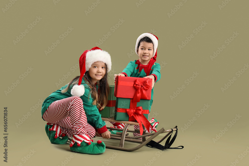 Cute little children with Christmas gifts and sleigh on green background