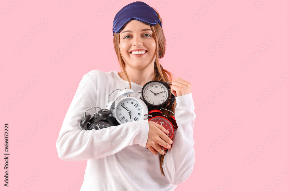 Happy young woman with alarm clocks on pink background