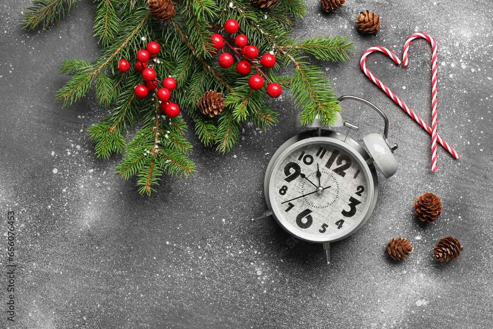 Alarm clock with Christmas tree branches and candy canes on grey background