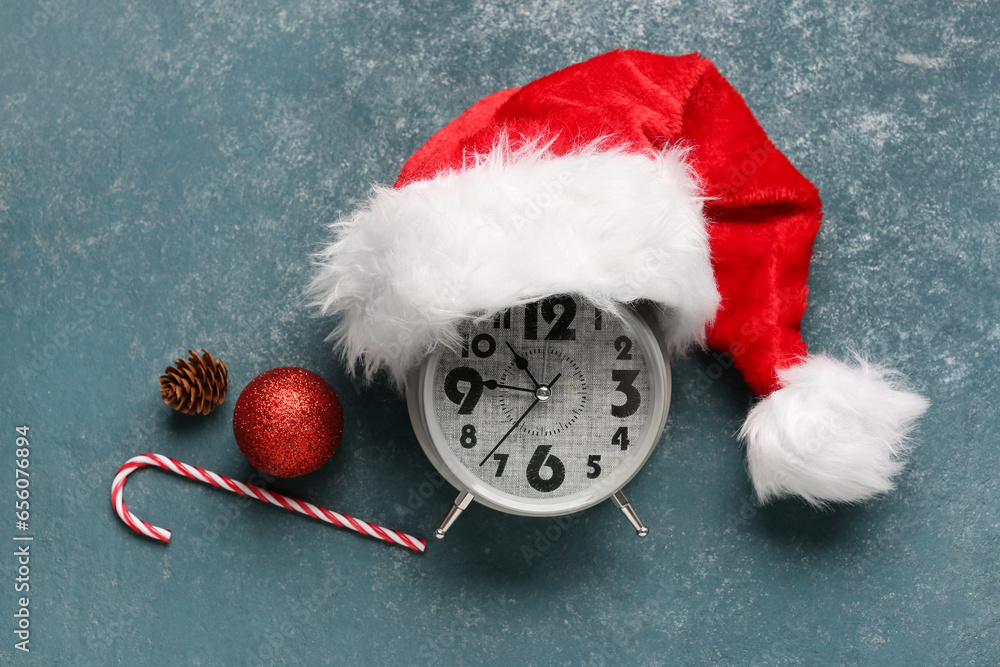 Alarm clock with Santa hat, Christmas ball and candy cane on blue background